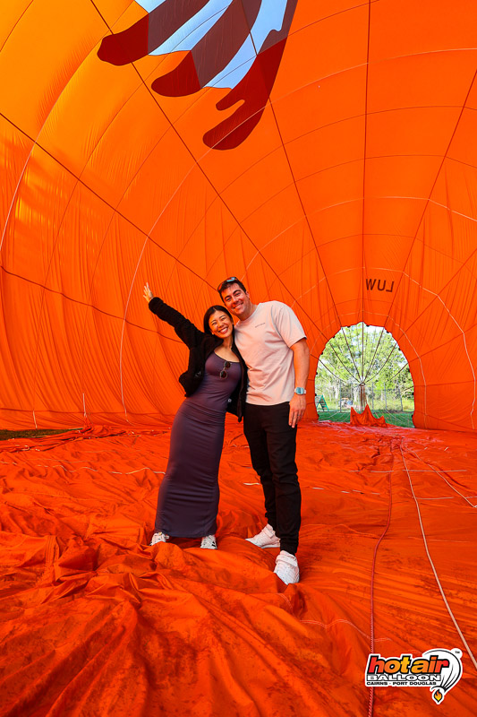Jocelyn and Brent standing inside the deflated hot air balloon envelope after their flight over the Atherton Tablelands, surrounded by the vivid orange fabric