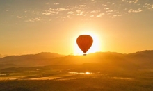Morning sun behind a hot air balloon with a mountain backdrop