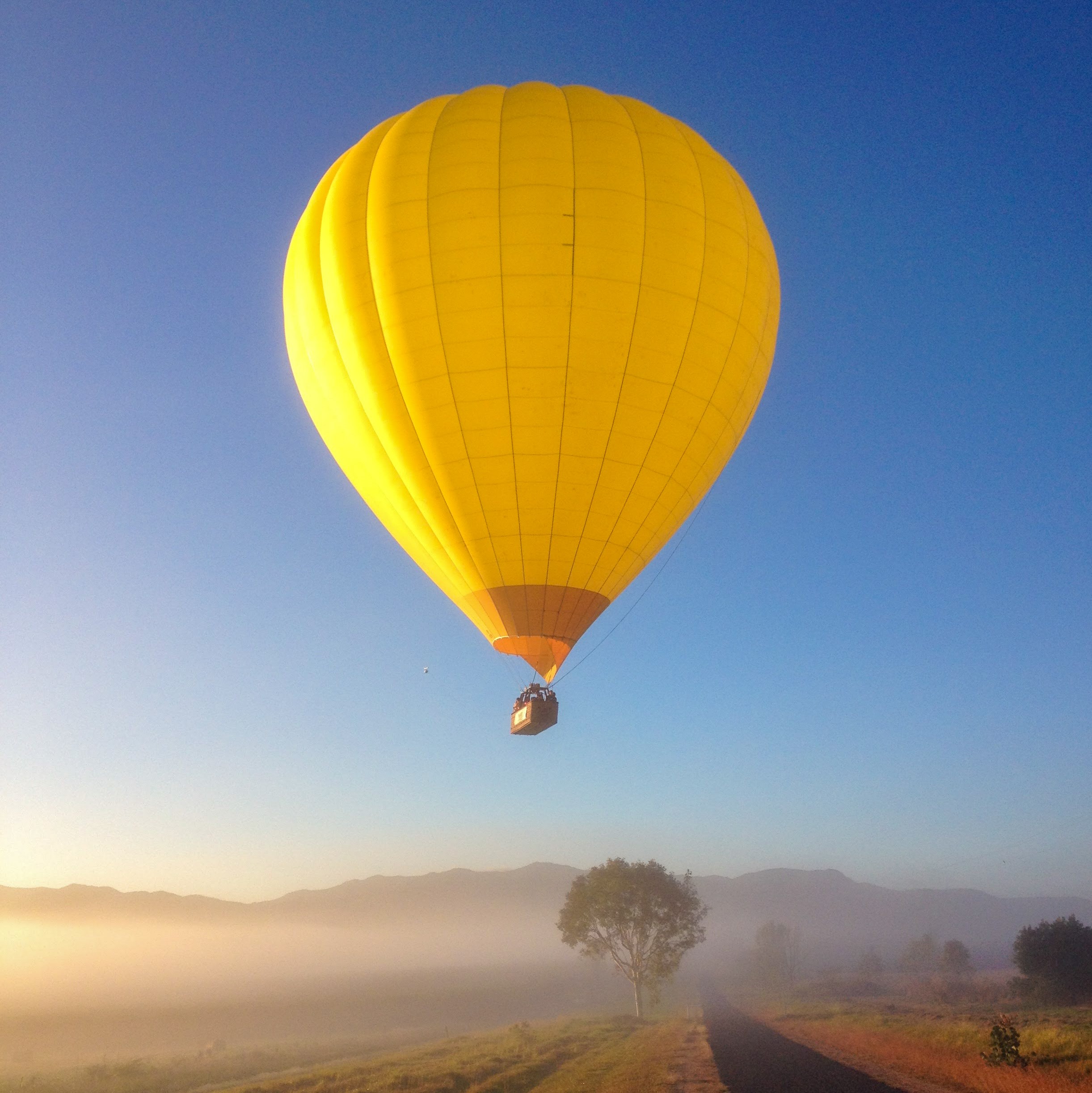 Yellow hot air balloon flying over a misty landscape